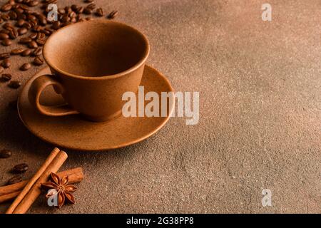 Leere Tasse und Untertasse aus Keramik, Kaffeebohnen, Zimt und Anise auf einer Steinoberfläche. Auf der rechten Seite befindet sich eine leere Werbefläche Stockfoto