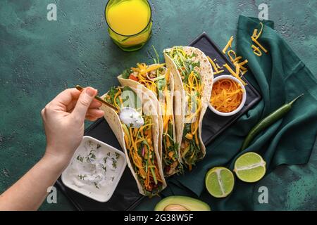 Frau bereitet leckere Tacos und Sauce auf farbigem Hintergrund Stockfoto