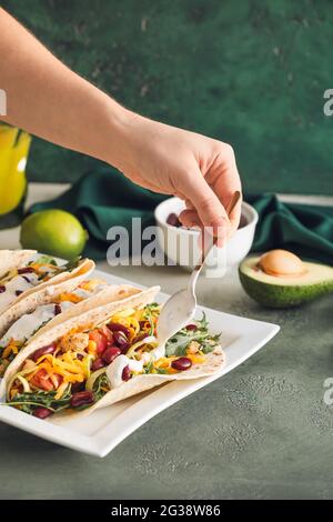 Frau kocht leckere Tacos auf farbigem Hintergrund Stockfoto