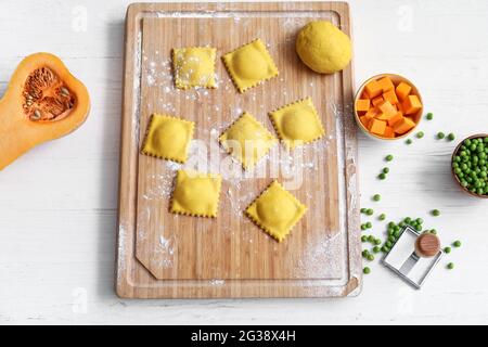 Holzbrett mit rohen Ravioli auf weißem Tisch Stockfoto