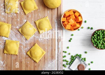 Holzbrett mit rohen Ravioli auf weißem Tisch Stockfoto