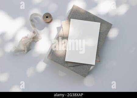 Sommer Hochzeit Schreibwaren Stillleben Szene. Altes Buch, leere Grußkarte, Einladungsmockup und Bastelumschlag im Sonnenlicht. Weißer Tischhintergrund Stockfoto