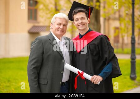 Glücklicher junger Mann mit seinem Vater am Abschlusstag Stockfoto