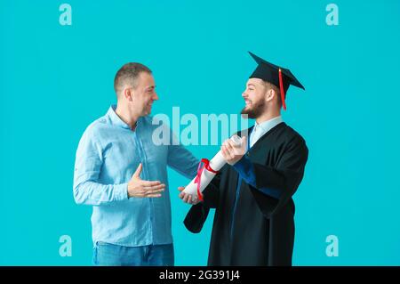Glücklich männlichen Abschluss Student mit seinem Vater auf farbigem Hintergrund Stockfoto