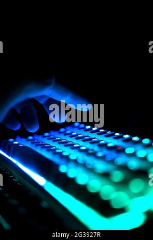 Perspektivische Seitenansicht Detailansicht Nahaufnahme der männlichen Finger, die auf der beleuchteten RGB-Gaming-Tastatur mit Tastenkappen tippen, die in blau und grün c leuchten Stockfoto