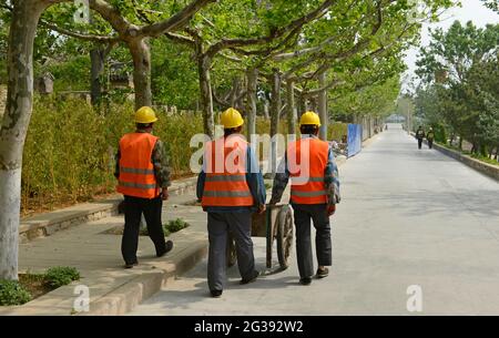 Arbeiter gehen auf der Liugong Insel vor der Küste von Weihai, China, während Renovierungsarbeiten an den vielen historischen Gebäuden auf der Insel entlang eines Pfades. Stockfoto