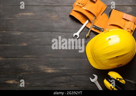 HardHat mit Baumaterial auf dunklem Holzhintergrund Stockfoto