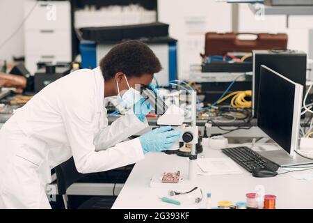 Wissenschaftlerin afroamerikanische Ingenieurin, die im Labor mit elektronischen Instrumenten und Mikroskop arbeitet. Forschung und Entwicklung von elektronischen Geräten durch schwarze Frau. Stockfoto