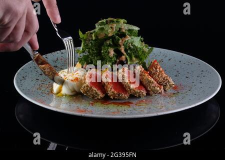 Thunfischsalat mit pochiertem Ei auf schwarzem Hintergrund Stockfoto