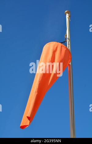 Leuchtend orangefarbene Windsocke, die im Wind gegen einen schlichten blauen Himmel weht Stockfoto