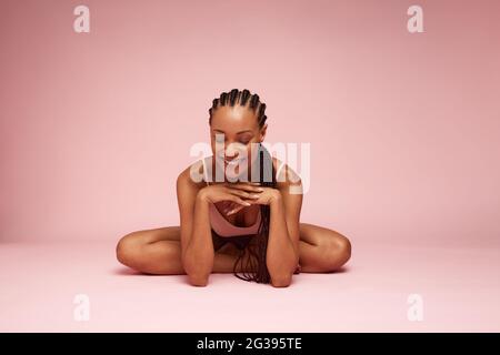 Frau, die mit der Hand auf dem Kinn sitzt. Weibliche Modell mit geflochtenen Frisur sitzt auf rosa Hintergrund und lächelt. Stockfoto