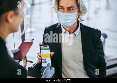 Der Reisende zeigt seinen Gesundheitspass der Impfbescheinigung telefonisch dem Sicherheitspersonal am Check-in-Schalter am Flughafen vor. Geschäftsmann zeigt seine va Stockfoto
