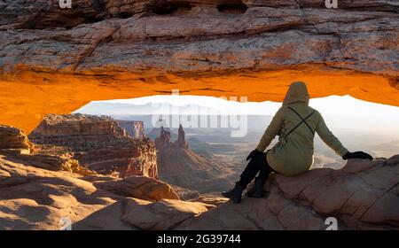 Frau, die den Mesa Arch bei Sonnenaufgang im Canyonlands National Park, Utah, USA, betrachtet Stockfoto