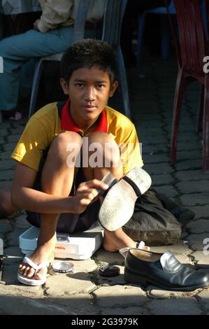 Ein Junge, der Schuhe putzt, auf einem Bürgersteig, in der Stadt Phnom Penh. In der Regel gehen Kinder aus ärmeren Gemeinden durch die Stadt, um ihren Lebensunterhalt zu verdienen, indem sie einen Schuhputzservice anbieten. Phnom Penh, Kambodscha. 20. Juni 2006. Stockfoto