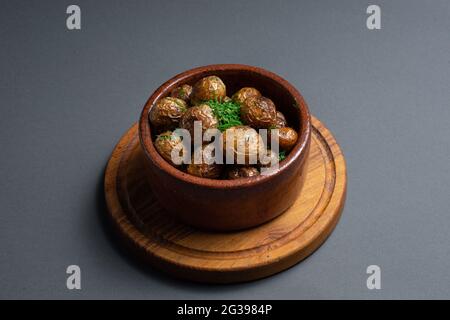 Nahaufnahme von gerösteten Kartoffeln mit Kräutern in Tonschüssel auf schwarzem Hintergrund Stockfoto