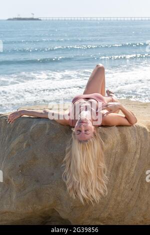 Schöne blonde Haare weibliche Modell auf dem Stein liegend mit Blick auf die Wellen mit geschlossenen Augen, während die Haare hängen. Stockfoto
