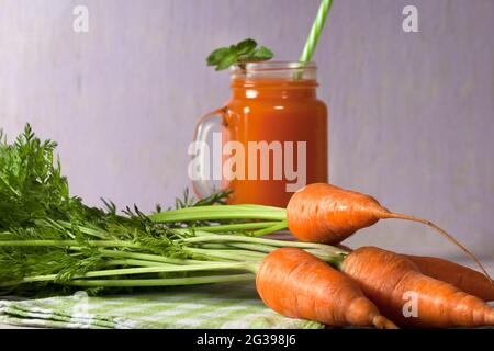 Köstlicher und gesunder Saft junger Karotten. Orangengetränk. Karottensaft. Frische Karotten mit grünen Blättern. Gesunde Ernährung. Stockfoto