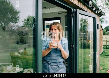 potter lächelt während einer Teepause während der Arbeit im Heimstudio Stockfoto