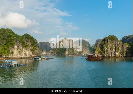 Eine Reihe schwimmender Häuser auf dem Wasser und ein vorbeifahrender Ausflugsboot in der Ha Long Bay, Vietnam Stockfoto