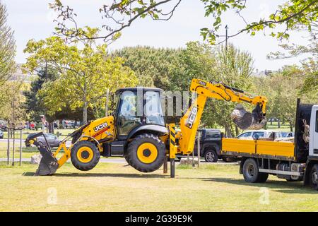 Ein gelber JCB 3CX Eco Baggerlader, der in einem Park in Southsea, Portsmouth, Hampshire, Südküste Englands, arbeitet, hob sich auf seinen Stützbeinen Stockfoto