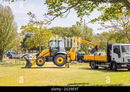 Ein gelber JCB 3CX Eco Baggerlader, der in einem Park in Southsea, Portsmouth, Hampshire, Südküste Englands, arbeitet, hob sich auf seinen Stützbeinen Stockfoto