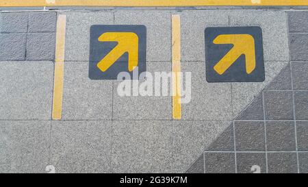 Pfeilschild in gelber Farbe auf schwarz auf der Wartelzone für Zug, U-Bahn gemalt Stockfoto