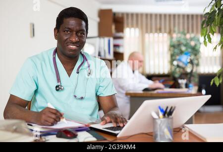 Lächelnde afroamerikanische Therapeutin, die im Büro mit einem Laptop arbeitet Stockfoto