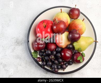 Rohe Früchte - Äpfel, Birnen, Pflaumen und Stachelbeeren auf einem runden Teller auf hellgrauem Hintergrund. Draufsicht, flach liegend Stockfoto