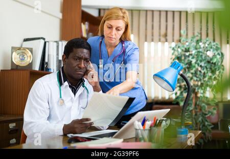 Porträt zweier multinationaler Ärzte im Büro, die aktuelle Fragen am Arbeitsplatz diskutieren Stockfoto