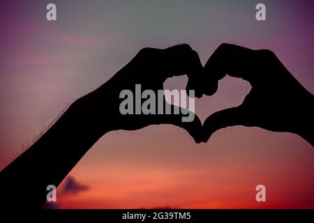 Liebeszeichen. Herz-Symbol von Hand Silhouette in Sonnenuntergang Himmel. Hintergrund im Vintage-Stil Stockfoto
