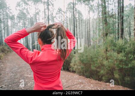 Läuferin Frau, die sich zum Laufen bereit macht, Haare ziehen, um einen Pferdeschwanz zu machen, um sich auf Langstreckenläufer in der Natur des Waldes vorzubereiten. Athletin aus Stockfoto