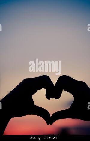 Liebeszeichen. Herz-Symbol von Hand Silhouette in Sonnenuntergang Himmel. Hintergrund im Vintage-Stil Stockfoto