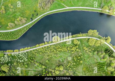 Wanderwege, die durch grünes Gras am Flussufer verlaufen. Sommerparklandschaft. Luftaufnahme. Stockfoto