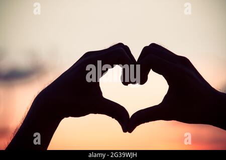 Liebeszeichen. Herz-Symbol von Hand Silhouette in Sonnenuntergang Himmel. Hintergrund im Vintage-Stil Stockfoto