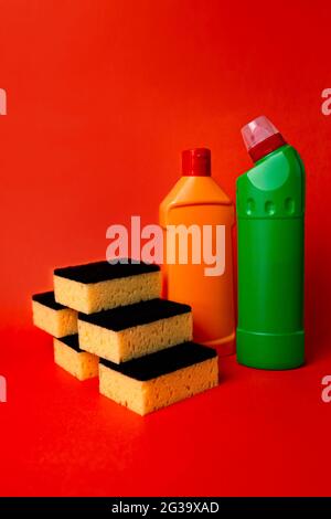 Schwämme und Reinigungsmittel in Flaschen auf rotem Hintergrund. Stockfoto