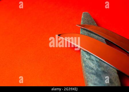 Messer schärfen und Stein zum Schärfen von Messern auf rotem Hintergrund Stockfoto
