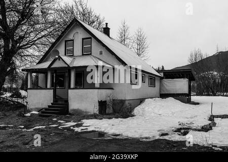 REVELSTOKE, KANADA - 14. MÄRZ 2021: Schwarz-weißes altes Haus in einer Kleinstadt Abendzeit früher Frühling mit Schnee Stockfoto