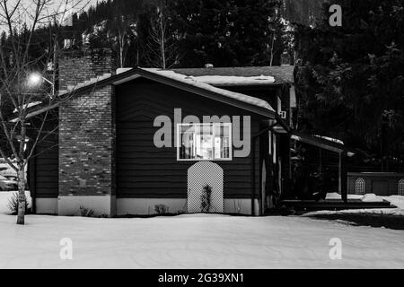 REVELSTOKE, KANADA - 14. MÄRZ 2021: Schwarz-weißes Privathaus in Kleinstadt Abendzeit früher Frühling mit Schnee Stockfoto