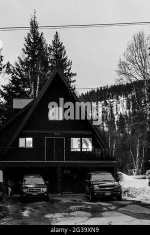 REVELSTOKE, KANADA - 14. MÄRZ 2021: Schwarz-weißes Privathaus in Kleinstadt Abendzeit früher Frühling mit Schnee Stockfoto