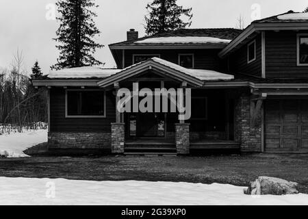 REVELSTOKE, KANADA - 14. MÄRZ 2021: Schwarz-weißes Privathaus in Kleinstadt Abendzeit früher Frühling mit Schnee Stockfoto