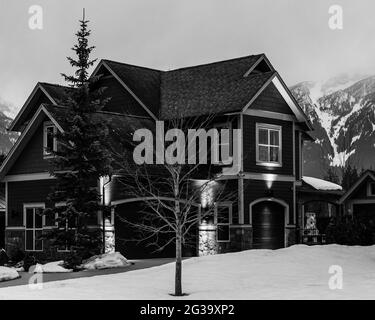 REVELSTOKE, KANADA - 14. MÄRZ 2021: Schwarz-weißes Privathaus in Kleinstadt Abendzeit früher Frühling mit Schnee Stockfoto