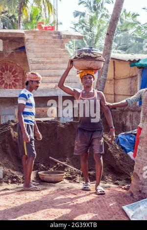 Männliche Arbeiter, die schwere Lasten auf dem Kopf tragen, posieren für Fotos auf der Baustelle, Agonda, Goa, Indien Stockfoto