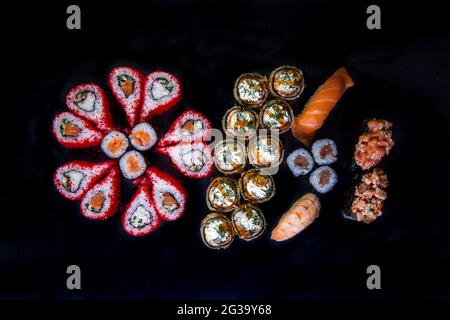 Großes Set mit Sushi und Rollen japanischer Küche, Draufsicht auf schwarzem Hintergrund. Stockfoto