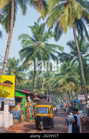 Auto Rickshaw Fahren Sie entlang der farbenfrohen Agonda Beach Road mit Palmen und blauem Himmel über Agonda, Goa, Indien Stockfoto