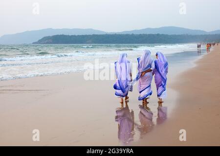 Rückansicht von drei katholischen Nonnen, die barfuß im nassen Sand am Strand entlang gehen, Agonda, Goa, Indien Stockfoto