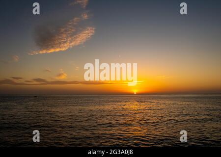 Orangefarbener und violetter Sonnenuntergang über dem Roten Meer und den sudanesischen Bergen am Horizont, ruhiger Abend, von einem Schiff aus gesehen, mit Zirruswolken am Himmel. Stockfoto