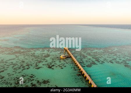 Sanganeb Reef National Park im Sudan, Rotes Meer, Luftaufnahme vom Sanganeb Lighthouse mit altem hölzernen Pier, der sich zum Meer hin erstreckt, azurblauem Kristallwasser Stockfoto