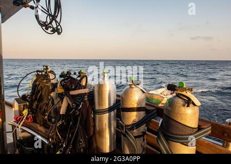 Tauchausrüstung mit Tanks, BCDs, Regulatoren, Gewichtsgurte montiert, auf einem Tauchboot mit Meerblick im Hintergrund, Rotes Meer, Sudan. Stockfoto