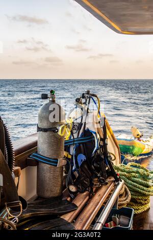 Tauchausrüstung mit Tanks, BCDs, Regulatoren, Gewichtsgurte montiert, auf einem Tauchboot mit Meerblick im Hintergrund, Rotes Meer, Sudan, Portraitansicht. Stockfoto