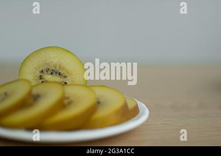 Goldene Kiwi-Scheiben mit gelbem Fruchtfleisch auf weißem Teller in der Küche. Exotische Früchte, gesunde Ernährung Konzept Stockfoto
